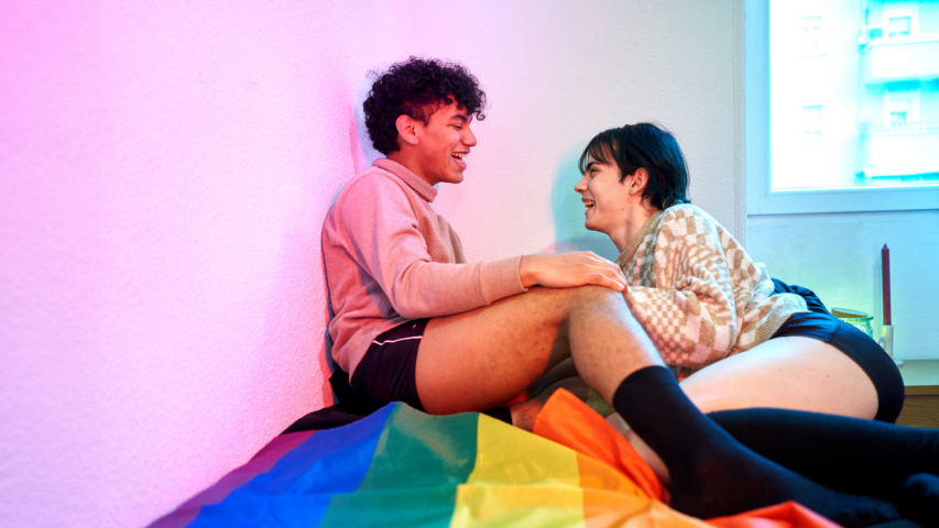 Two people having a lively conversation while sitting on a Pride flag. 