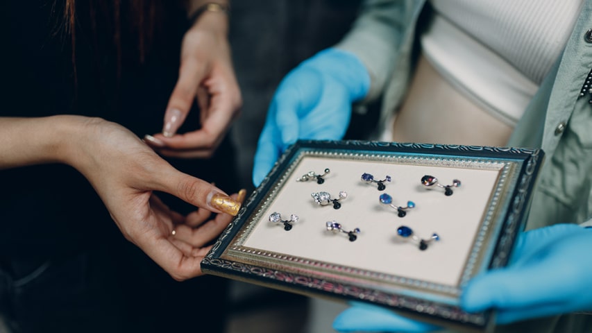 Piercer wearing medical gloves showing their client a variety of vaginal piercing jewellery options.