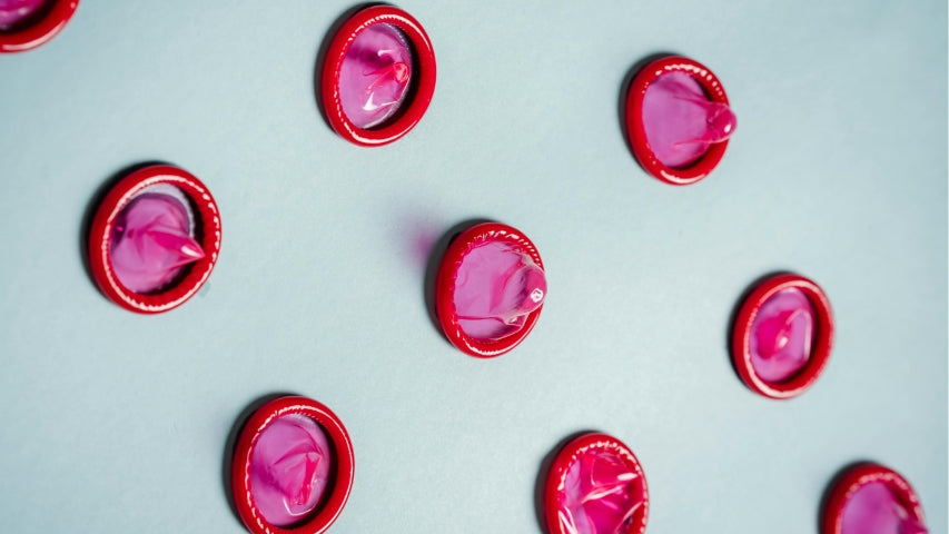 Rows of individual pink and red condoms spread out on a white board.