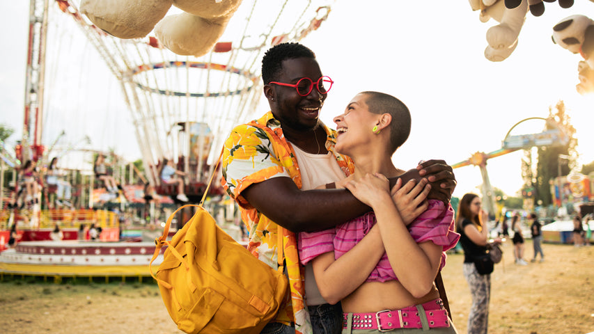 Couple wearing bright colours embracing each other and laughing at an outdoor carnival. 