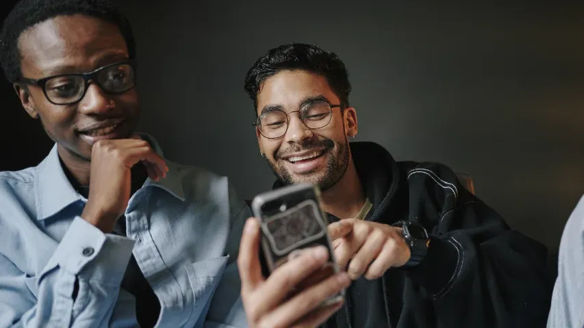 Two men sitting together, one showing something on his phone while the other watches with interest.